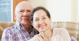 An elderly man and woman sitting cuddled on a couch